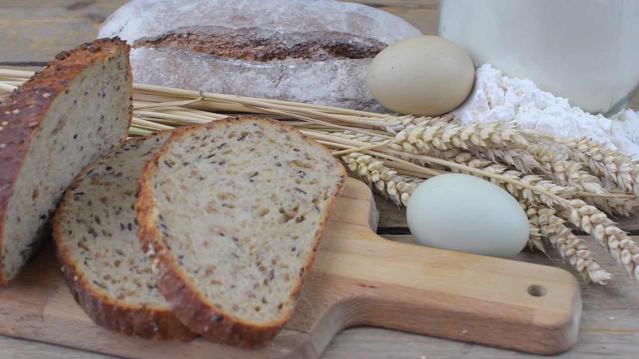 Loafs of bread, slices of bread, wheat flour, eggs and ears of grain on wood background. Rustic and rural concept. Close up. Flat lay