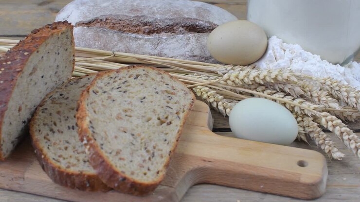 Loafs of bread, slices of bread, wheat flour, eggs and ears of grain on wood background. Rustic and rural concept. Close up. Flat lay