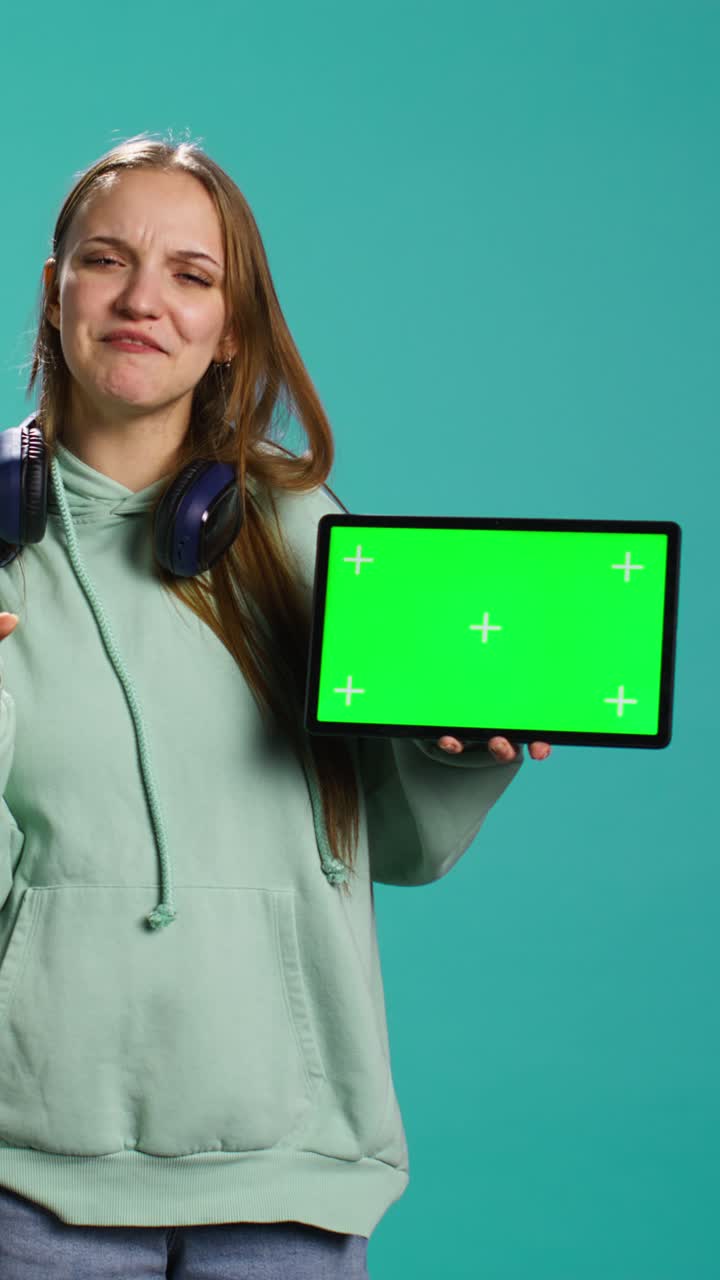 Video verticale: radiosa giovane ragazza che dà un feedback su un tablet con green screen