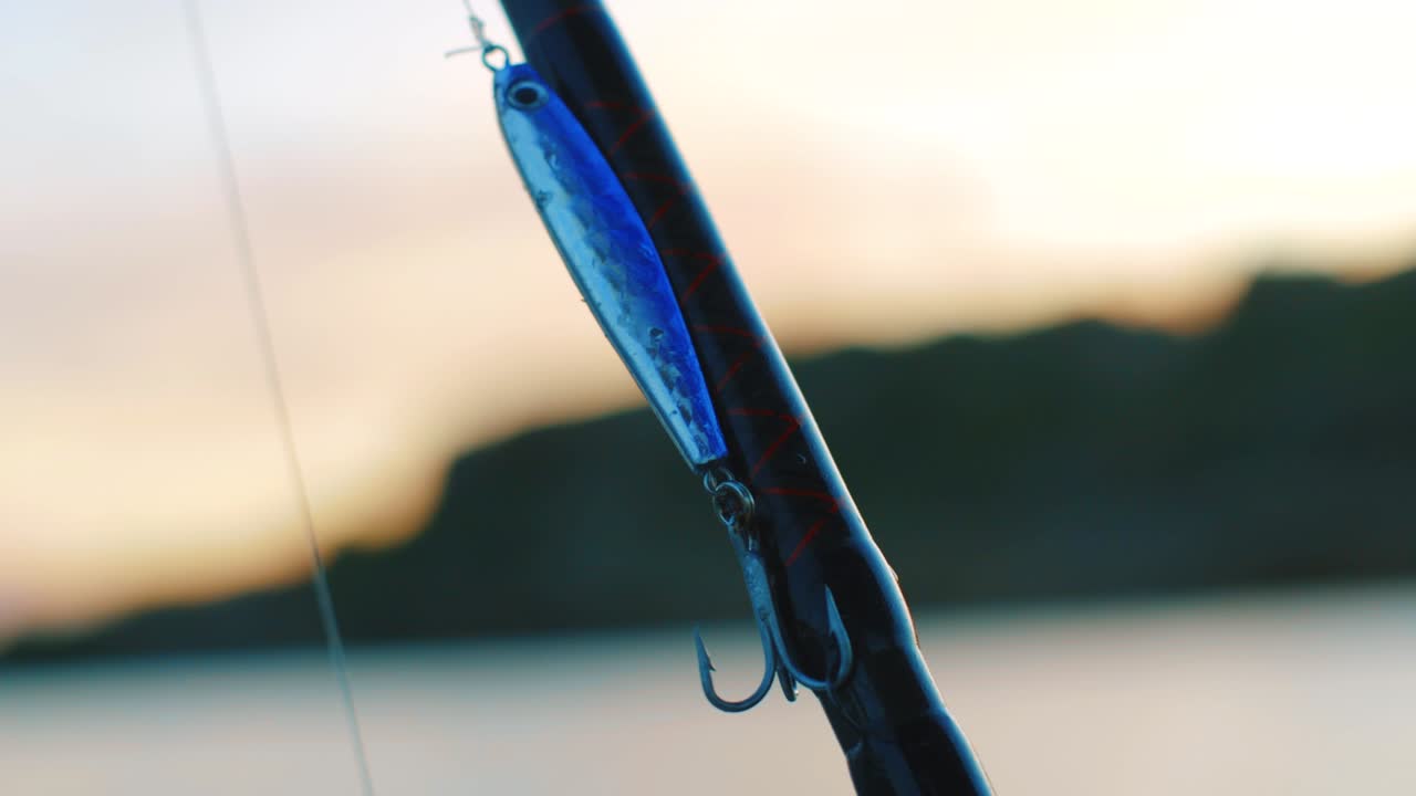 Metal fishing lure attached to fishing rod with beautiful sunset in the background