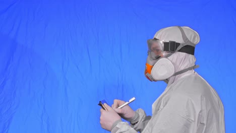 científico virólogo en respirador hace escribir en una tableta con lápiz. hombre con máscara médica protectora. clave de croma azul