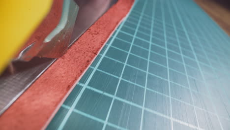 person cuts thin strip of red leather with knife on table