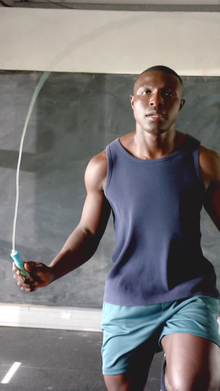 Vertical video: Athletic man jumping rope in gym, focused on fitness and endurance training