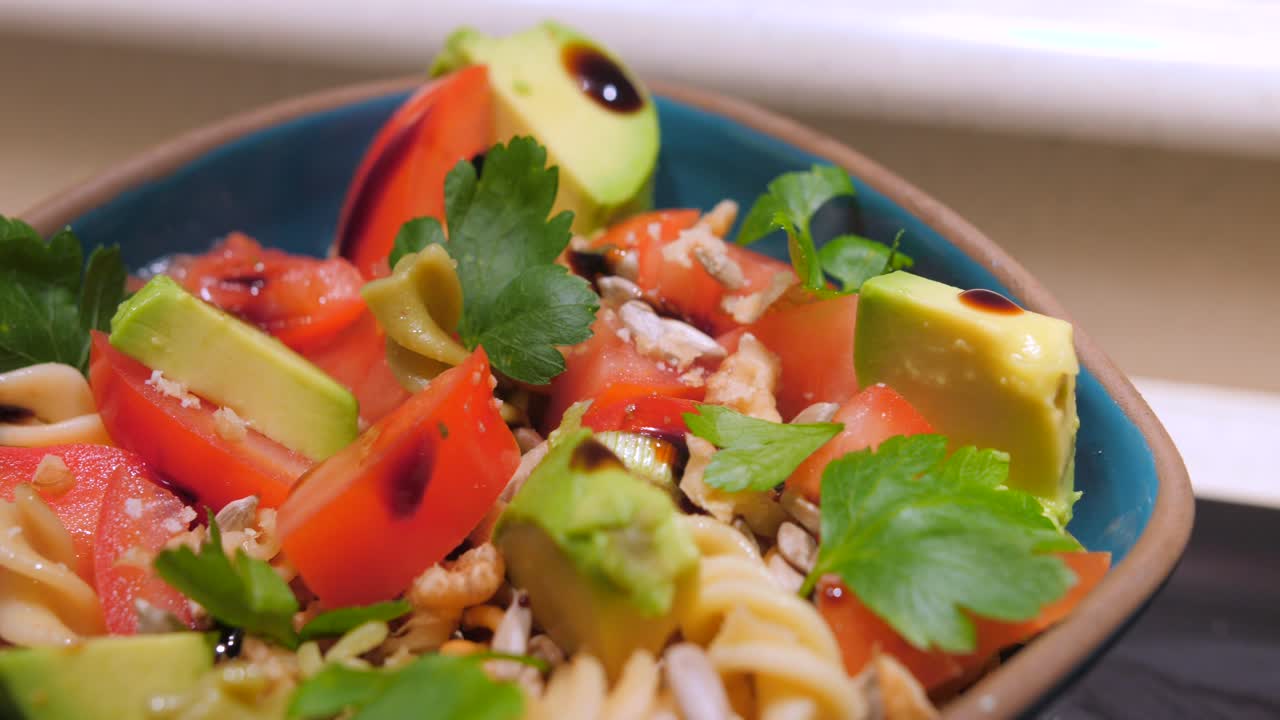 vista de cerca de la nutritiva ensalada de pasta con tomate, aguacate, pimientos, nueces y vinagre balsámico, servida en un tazón azul