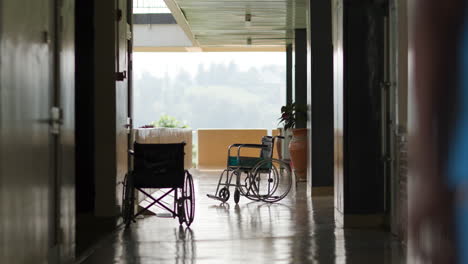 slow motion shot of nurse walking toward camera with two empty wheel chairs at end of hallway in rwandan hospital