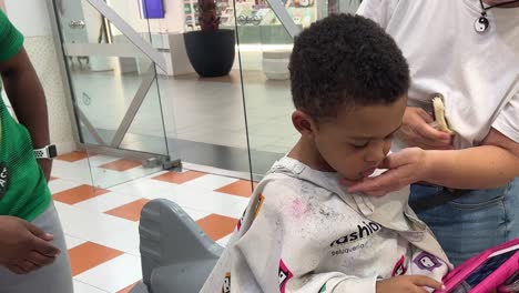 Cute-and-exotic-three-year-old-kid-after-getting-a-haircut-in-a-children’s-hair-saloon-while-his-mother-comforts-him