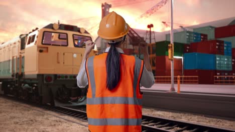back view of a female engineer with safety helmet raising her hands celebrating while working with freight cargo train at port