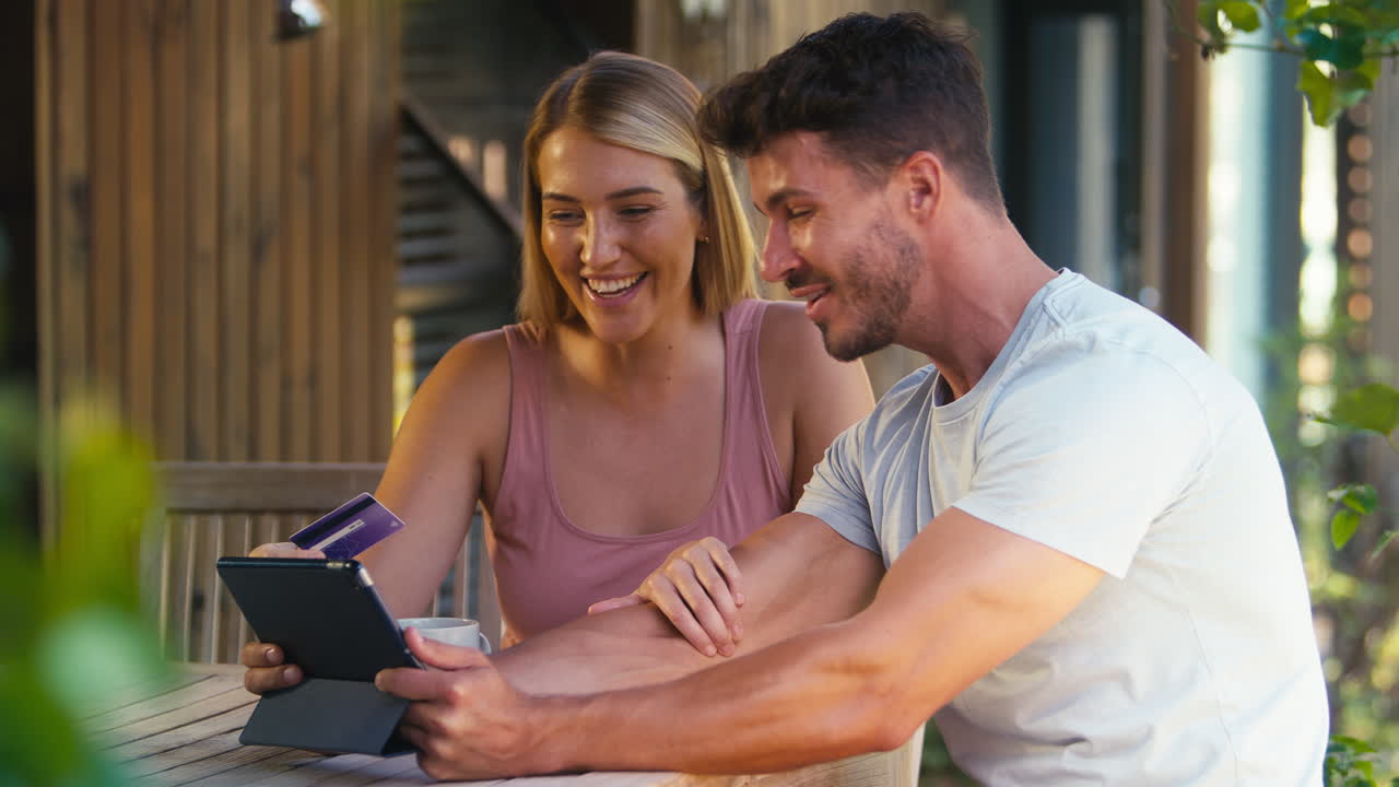 Excited Couple With Credit Card Using Digital Tablet At Home To Book Holiday Or Shop Online