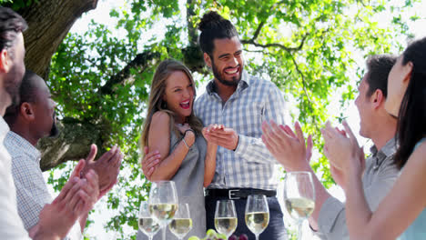 Happy-couple-embracing-while-friends-applauding-during-lunch