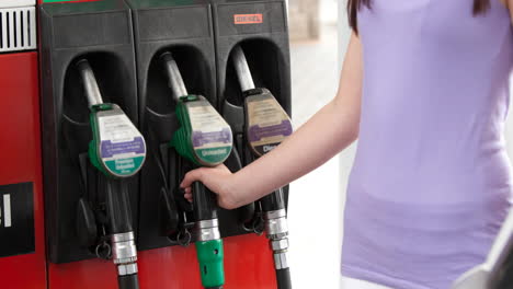 sección media de una mujer caucásica en top lila usando una bomba de combustible en una gasolinera