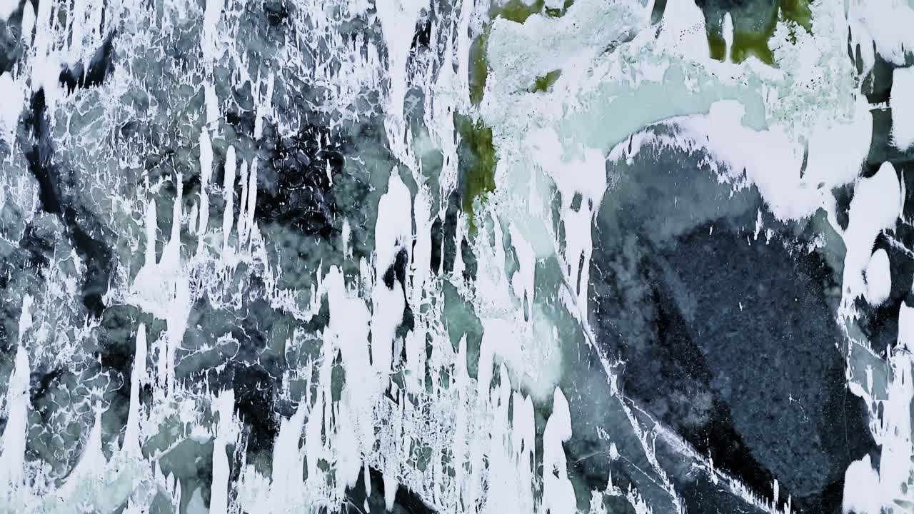 Veduta aerea dall'alto con drone di ghiaccio marino e acqua scura che formano motivi invernali astratti, con crepe, fanghiglia e striature di neve che creano una texture naturale ad alto contrasto.