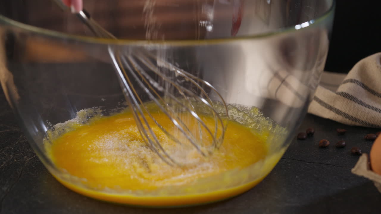 Mixing Sugar And Egg In A Glass Bowl With A Whisk. - closeUp shot