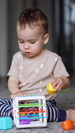 calm little boy plays on the floor. kid takes a toy out of cube and then stands up. blurred backdrop. vertical video