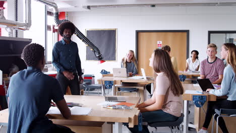 Teacher Talking To Group Of High School Students Sitting At Work Benches In Design And Technology Lesson