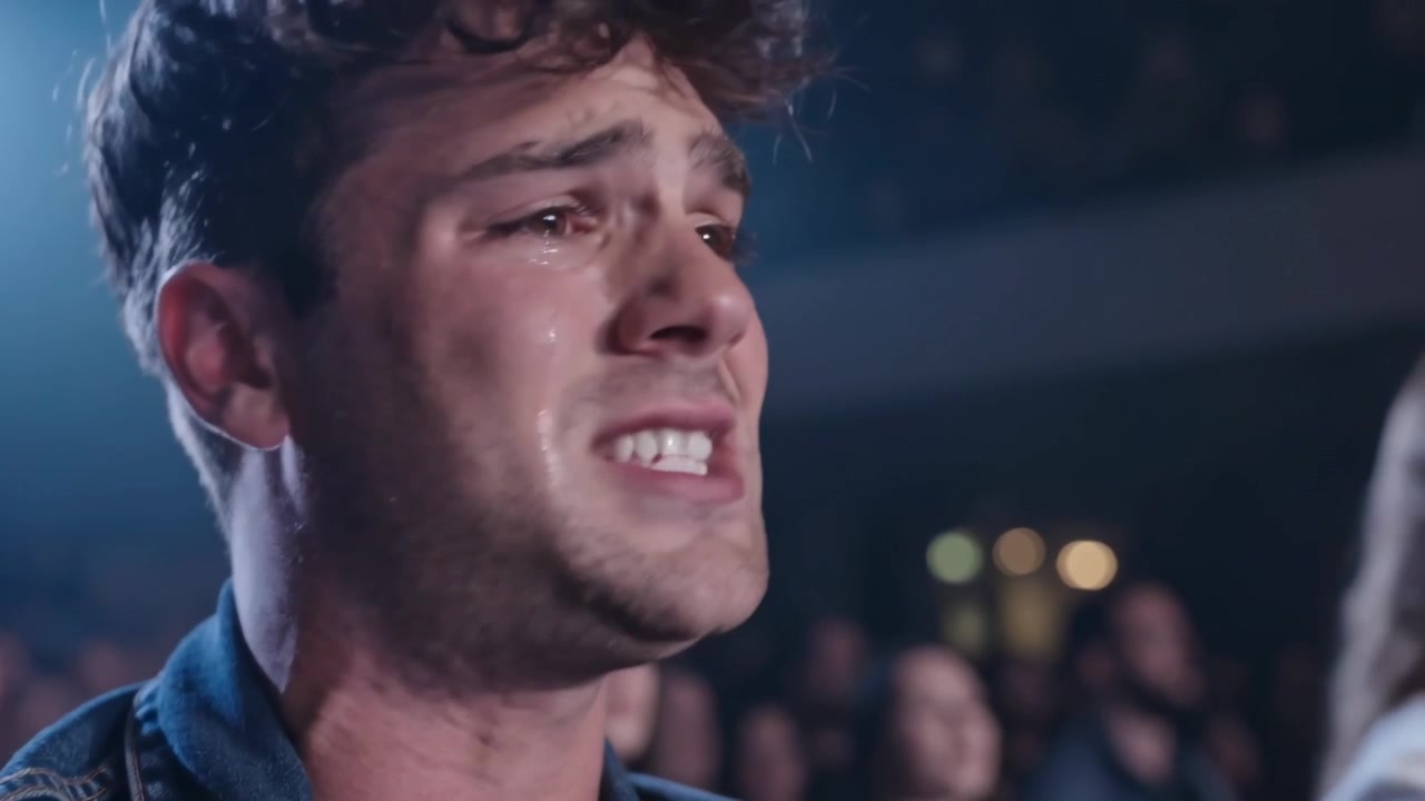 Fan maschio che canta a squarciagola con la musica che inizia nel locale, giacca di jeans, luce del palco, lacrime.