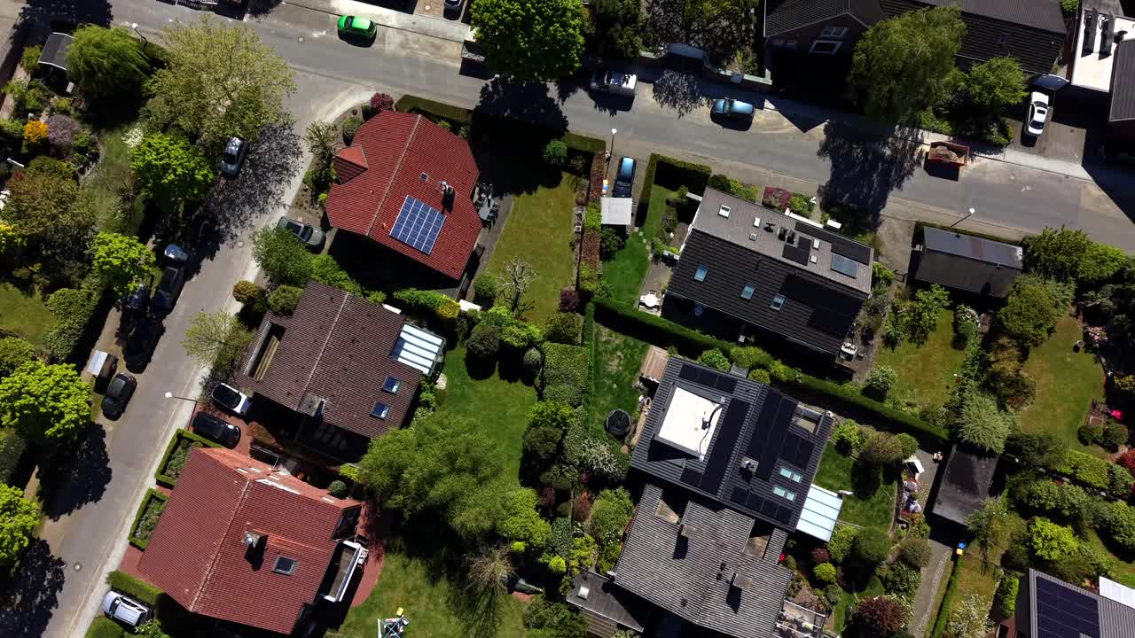 Vista aerea dall'alto di un tranquillo quartiere residenziale con tetti a pannelli solari, giardini verdi, strade alberate e case colorate sotto il luminoso sole primaverile. Ripresa in elevazione. Produzione di energia verde