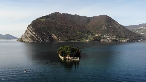 Drohne-Dreht-Sich-Um-Die-Insel-San-Paolo-Auf-Dem-Iseo-See-Und-Folgt-Einem-Boot,-Das-Den-Panoramasee-Enthüllt