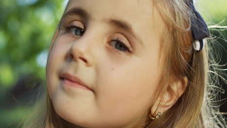 Close-up-view-of-blonde-and-cute-girl-looking-at-the-camera-in-the-park-on-a-summer-day