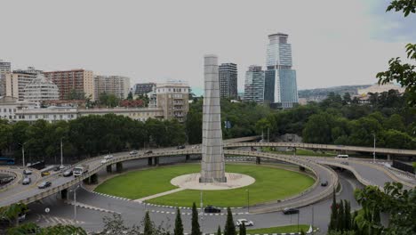 a bustling cityscape featuring contemporary high-rise buildings and a prominent circular monument in the foreground