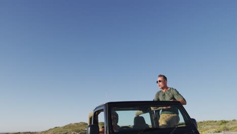 Glückliches-Kaukasisches-Schwules-Männliches-Paar-Im-Auto,-Das-Die-Aussicht-Bewundert-Und-An-Einem-Sonnigen-Tag-Am-Strand-Mit-Den-Armen-Winkt