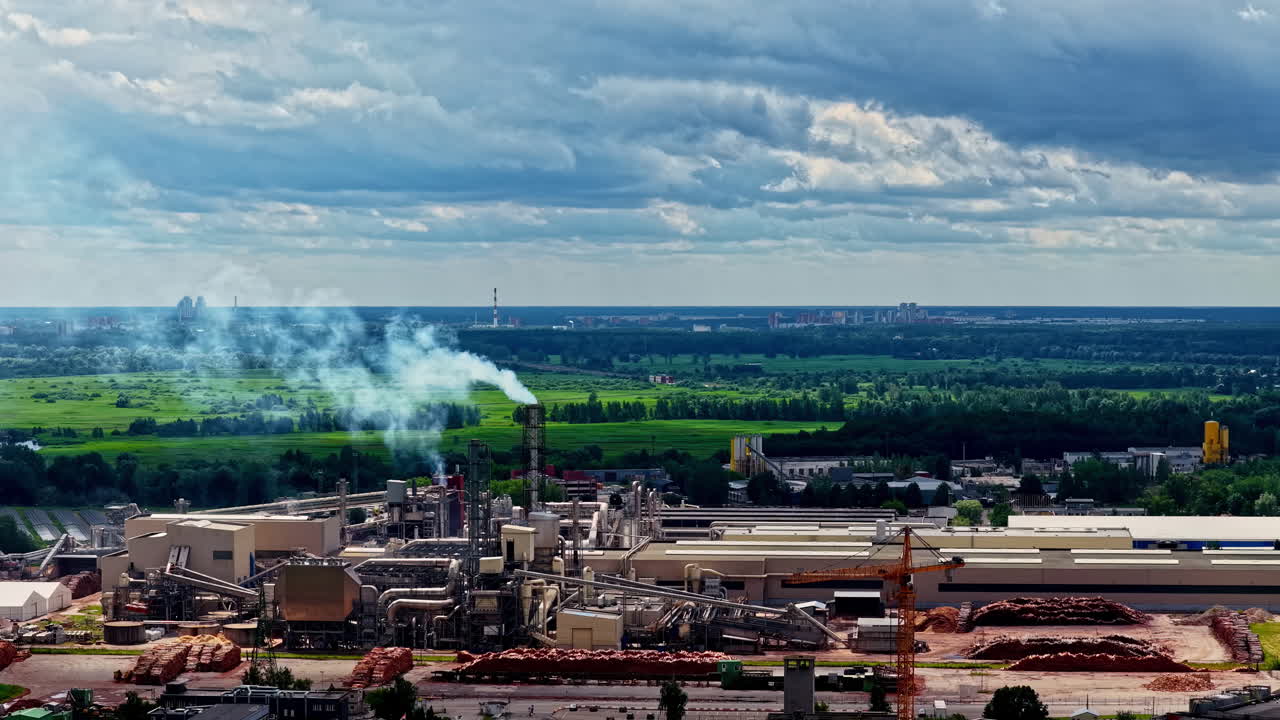 Smoke rising from sawmil factory complex in industrial zone with log piles in yard