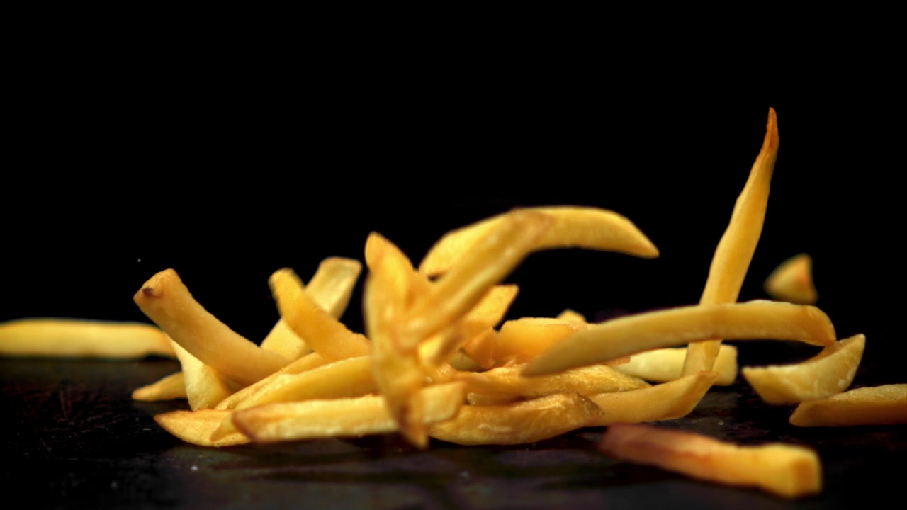 Golden French Fries Falling in Slow Motion on Black Background