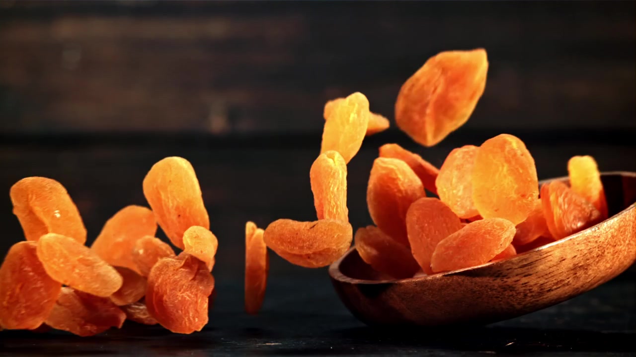 Dried Apricots Falling from a Wooden Spoon in Slow Motion
