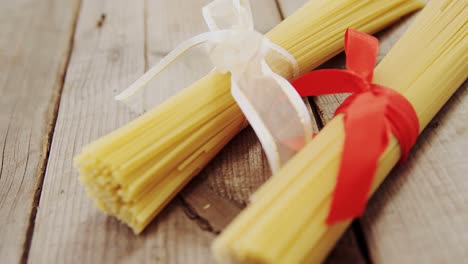 dos paquetes de pasta de espagueti atados con cintas rojas y blancas en un fondo de madera