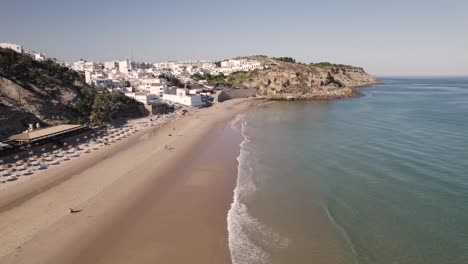 Breathtaking-aerial-view-of-Burgau-Portugal-splitting-between-aqua-green-ocean-and-whitewashed-stucco-buildings