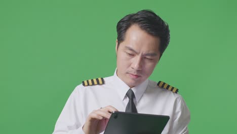 close up of asian man pilot taking note on a tablet while standing in the green screen background studio