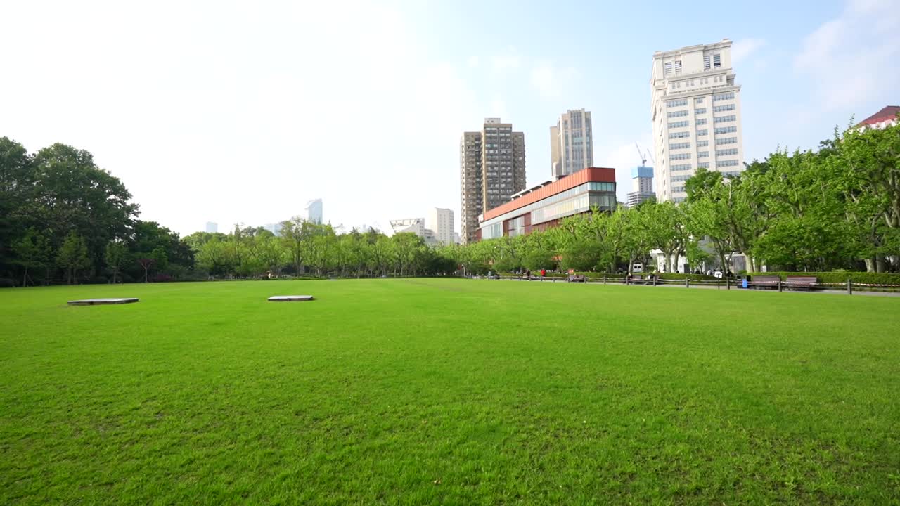 Panning right along a green meadow at Fuxing Park with residential towers rising in the background
