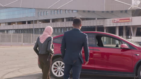 business couple outside red electric car