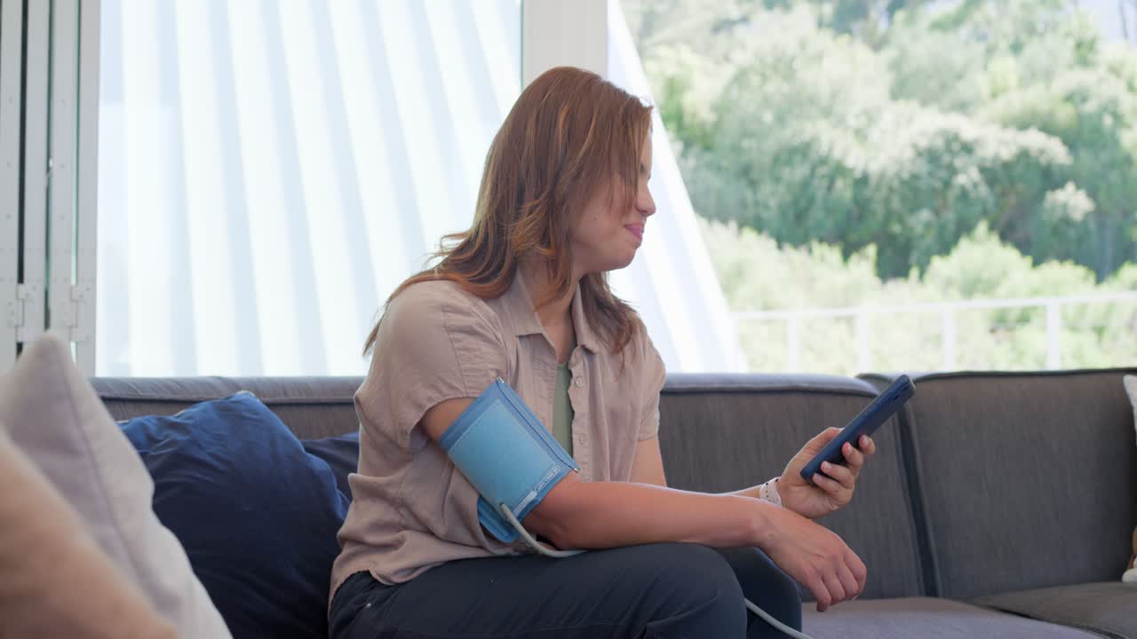 Donna afroamericana seduta sul divano dopo aver applicato il bracciale per la pressione sanguigna, sollevando il monitor e controllando la lettura.