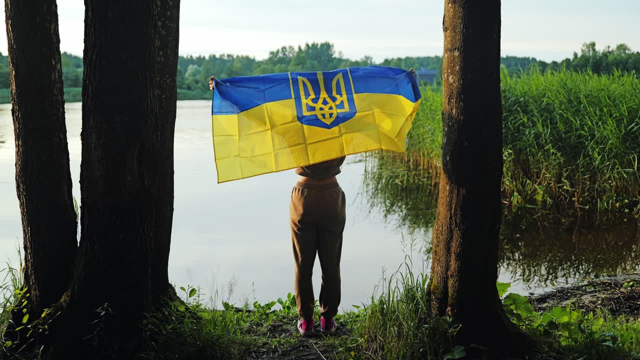 Symbolic slow motion of woman lifting Ukraine flag by river in peaceful dawn
