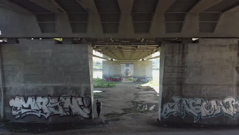 Aerial-drone-shot-of-under-the-bridge-while-a-person-carries-and-walks-looking-to-vista-river-Warsaw-Poland