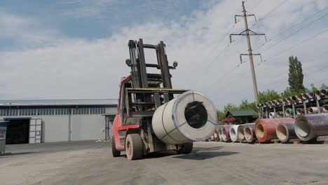 forklift driver loads rolls of steel sheet. industrial warehouse with rolls of steel sheet