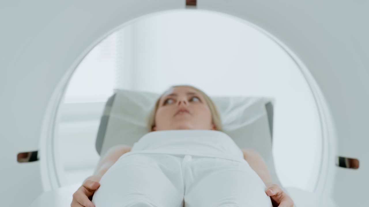 Ritratto ravvicinato di una paziente donna sdraiata per una TAC o una risonanza magnetica, il lettino si muove all'interno della macchina che scansiona il suo corpo e il suo cervello. In un laboratorio medico con attrezzature ad alta tecnologia. Si avvicina alla telecamera.