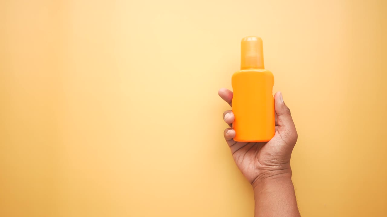 Hand holding a bottle of orange sunscreen