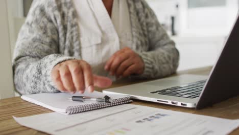 mid section of african american senior woman taking notes and using laptop at home