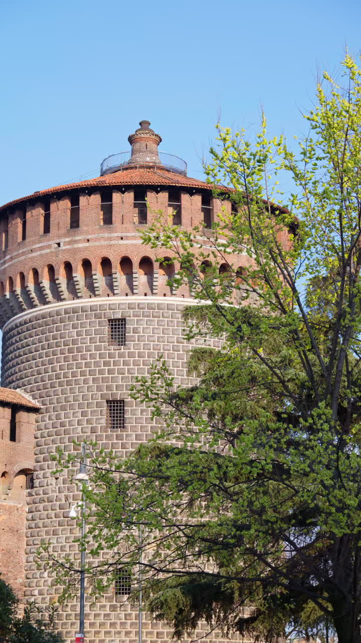 View of the Sforzesco Castle in Milan, Italy, surrounded by green trees on a blue sky background. Vertical