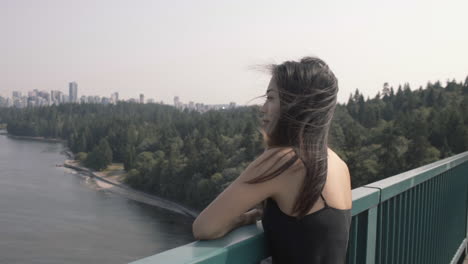 toma mediana de steadicam de una mujer asiática disfrutando de una hermosa vista de la entrada de burrard desde el puente lions gate, en cámara lenta