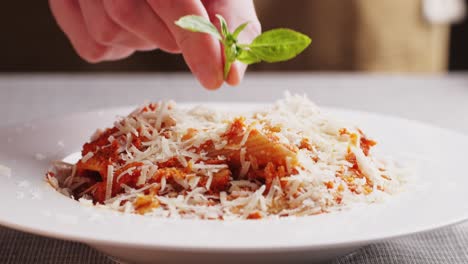 chef preparando un plato de pasta con parmesán y albahaca