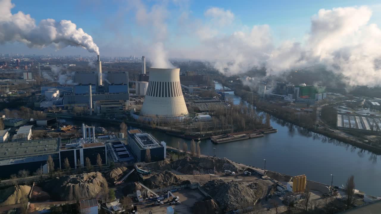 power plant emitting steam from its cooling tower, situated by a river and overlooking the cityscape. Majestic aerial view flight speed ramp hyper motion time lapse