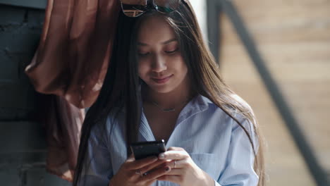 Chica-Con-Camisa-A-Rayas-Y-Gafas-De-Sol-Mira-La-Pantalla-Del-Teléfono-Inteligente-Mientras-Chatea