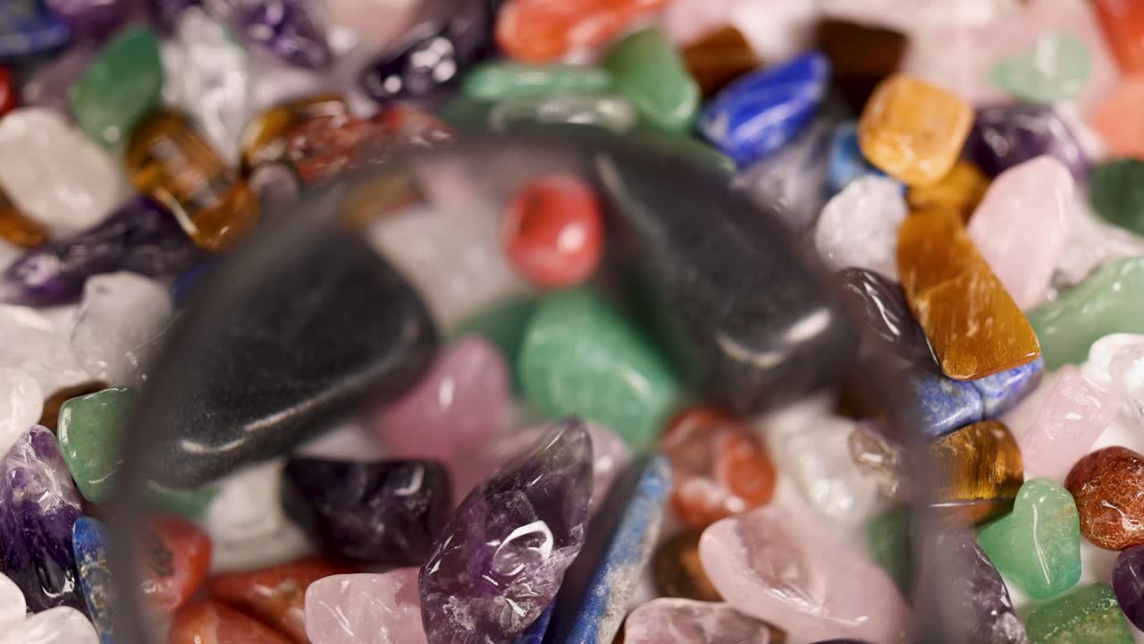 A magnifying glass moves over vibrant chakra stones, highlighting their colors and textures under bright lighting