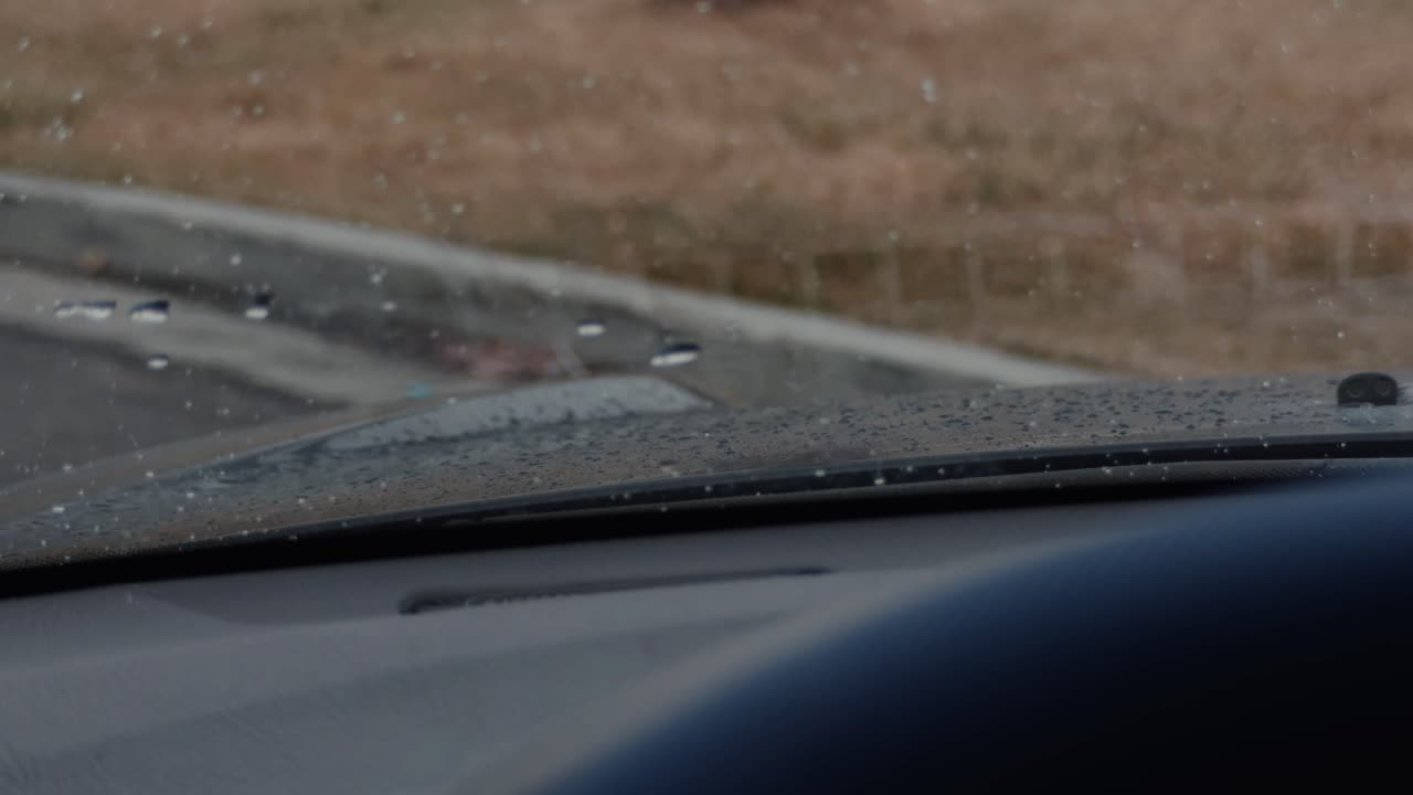 Zoomed in shot of a windshield with rain water droplets on a drizzling day.