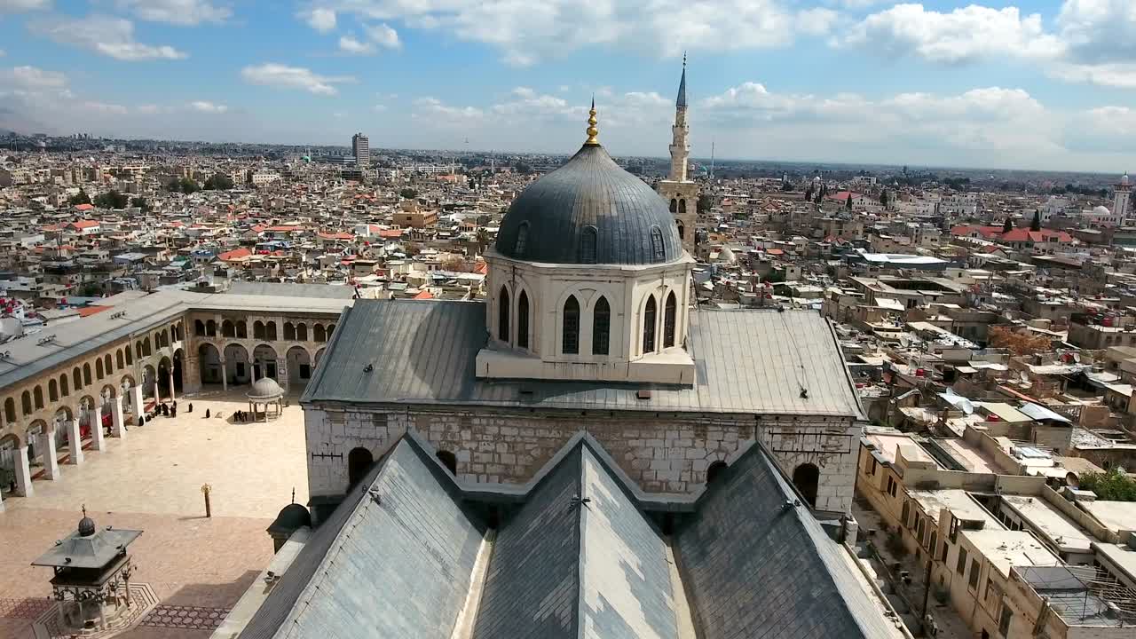 시리아의 우마야드 모스크 위의 공중 풍경: 무인기가 타워 모스크의 외부 건물을 돌아다니며 다마스쿠스 시를 배경으로 하고 있습니다.