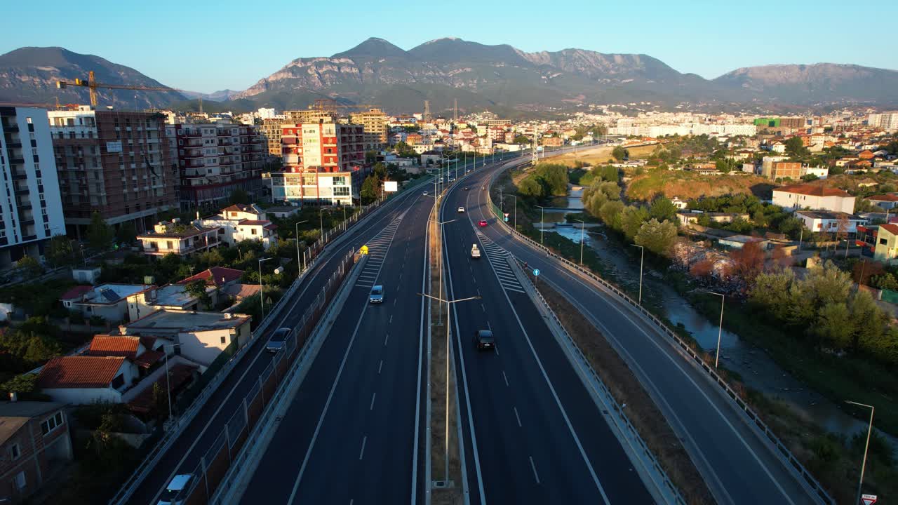 Highway lines of Tirana ring road at twilight with suburban buildings, mountains, cars, people, and destinations