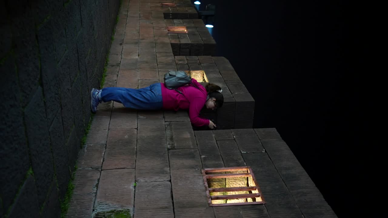 Caucasian woman taking pictures through a crenellated wall in Fenghuang Old Town at night