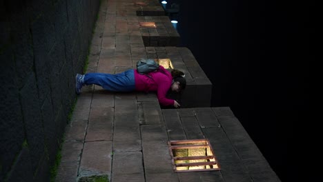 caucasian woman taking pictures through a crenellated wall in fenghuang old town at night